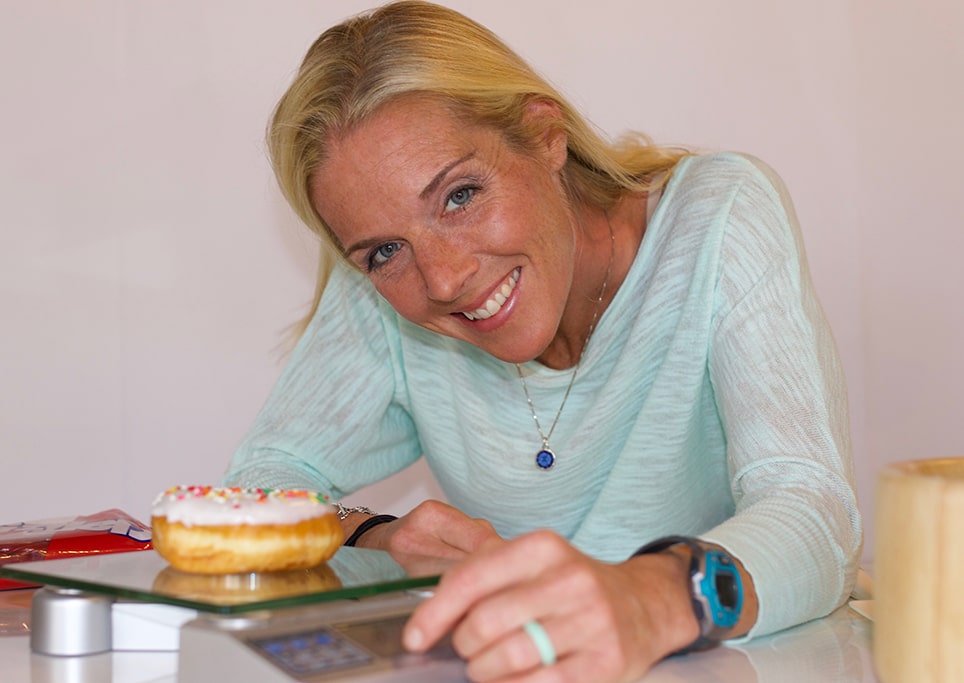 Dr. Tiff smiling wearing an ocean blue top. A doughnut is in the foreground on a food scale and in the background is a bag of Twizzlers candy